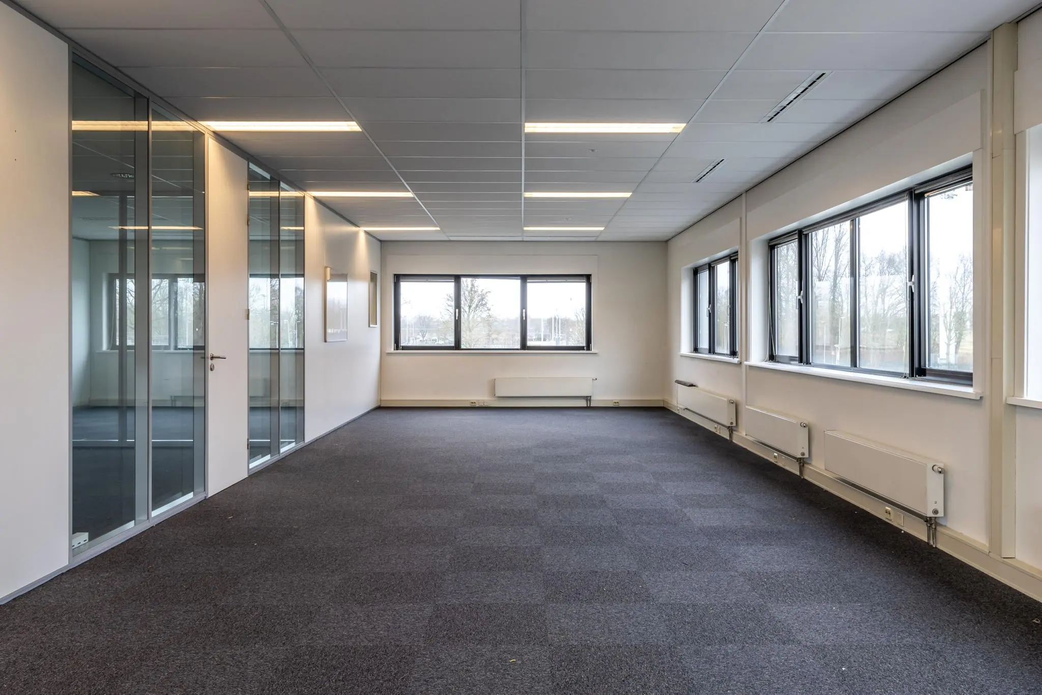 Licht en leeg kantoorruimte aan de Lage Biezenweg met grote ramen en glazen binnenwanden.